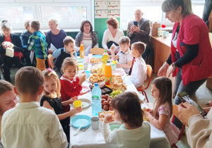 Dzieci z grupy biedronek siedzące przy wspólnym poczęstunku przy stołach.