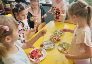Dzieci stojące przy stole. Własnoręcznie przygotowujące szaszłyki owocowe.