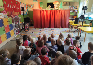 Dzieci z grupy biedronki,misie i motylki siedzące na dywanie podczas przedstawienia.