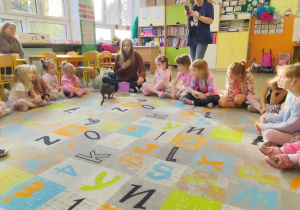 Dzieci siedzące na dywanie podczas spotkania z panią edukatorką.