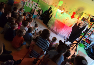 Dzieci siedzące na dywanie, oglądające przedstawienie.