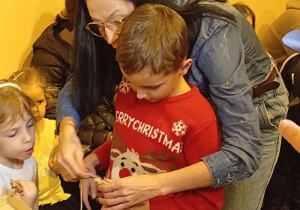 Chłopiec wykonujący wspólnie z wolontariuszem makramowe ozdoby.