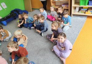 Dzieci z przedszkola siedzące na dywanie podczas trwającego przedstawienia.