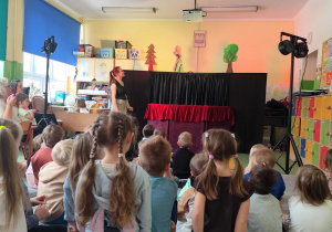 Dzieci z przedszkola siedzące na dywanie podczas trwającego przedstawienia.