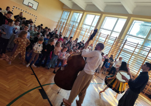 Dzieci z przedszkola stojące na sali gimnastycznej podczas koncertu muzycznego.