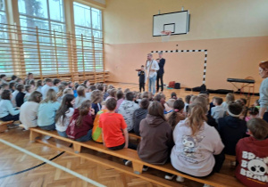 Dzieci siedzące na sali gimnastycznej podczas koncertu Akademii Pana Feliksa.