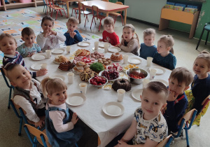 Grupka uśmiechniętych dzieci siedzi przy stole na stoliku potrawy wielkanocne.