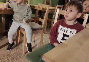 Chłopcy siedzą przy stoliku i oglądają przedstawienie.