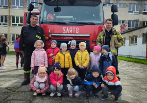 Grupa uśmiechniętych dzieci stoi przed wozem strażackim.