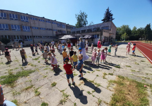 Grupa dzieci na placu przedszkolnym tańczących do muzyki.