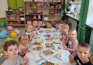 Grupka dzieci siedzących przy stole zajadająca się pysznymi przekąskami