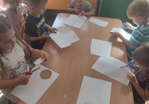 Grupka dzieci siedzących przy stole i wycinających koła z papieru