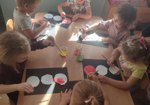 Grupka dzieci siedzących przy stole malująca farbami wycięte koła z papieru