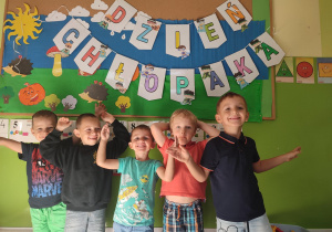 Grupka chłopców stojąca pod tablicą z napisem dzień chłopaka