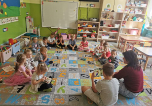Grupa dzieci siedzących na dywanie słuchających opowiadania czytanego przez starszego chłopca