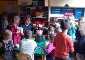 Grupa dzieci wraz z nauczycielem przy stoliku przygotowuje soczek owocowy