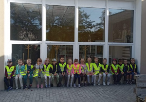 Grupa dzieci siedzących na murku pod miejską biblioteką