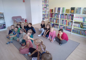 Grupa dzieci siedzących na dywanie w miejskiej bibliotece
