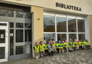Grupka dzieci siedzących na murku przed wejściem do biblioteki