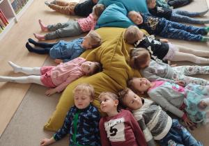 Grupka dzieci leżących na dywanie z głowami na poduszkach słuchających bajki czytanej przez bibliotekarkę