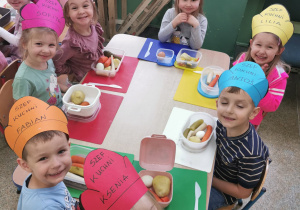 Grupka dzieci siedzących przy stole.Na stole leżą pudełeczka z ugotowanymi warzywami.