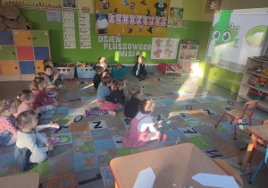 Grupka dzieci siedzących na dywanie przed tablicą interaktywną oglądająca film edukacyjny o kredkach.