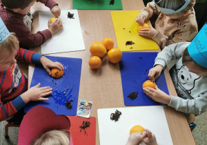 Grupa dzieci przy stole wykonująca jeżyki z pomarańczy i goździków.