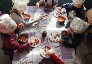 Grupa dzieci przy stoliku z produktami do przygotowania czekolady.
