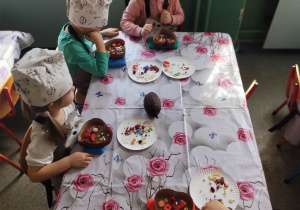 Grupa dzieci przy stoliku z produktami do przygotowania czekolady.