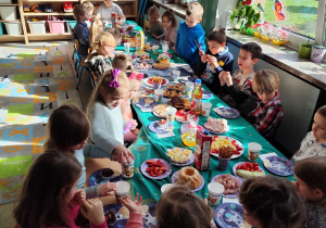 Grupa dzieci siedzących przy stołach podczas śniadanka wielkanocnego.